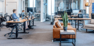 Modern office workspace with multiple desks, employees working on computers, and a lounge area featuring a plant and comfortable seating, reflecting a collaborative digital marketing environment.