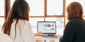 Two women collaborating on a laptop, discussing website design and digital marketing strategies in a bright, modern workspace.