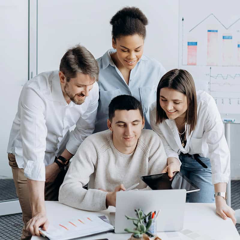 Group of professionals collaborating around a laptop, discussing website design and digital marketing strategies, with charts and graphs in the background.