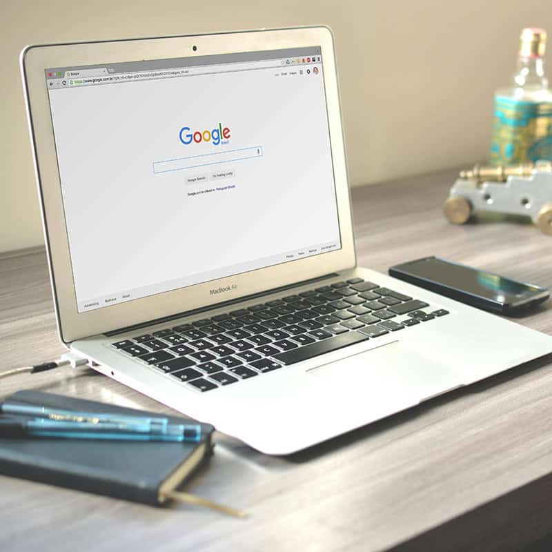 Laptop displaying Google search page on a wooden desk, with a smartphone and notebook nearby, symbolizing local SEO strategies for enhancing online visibility.
