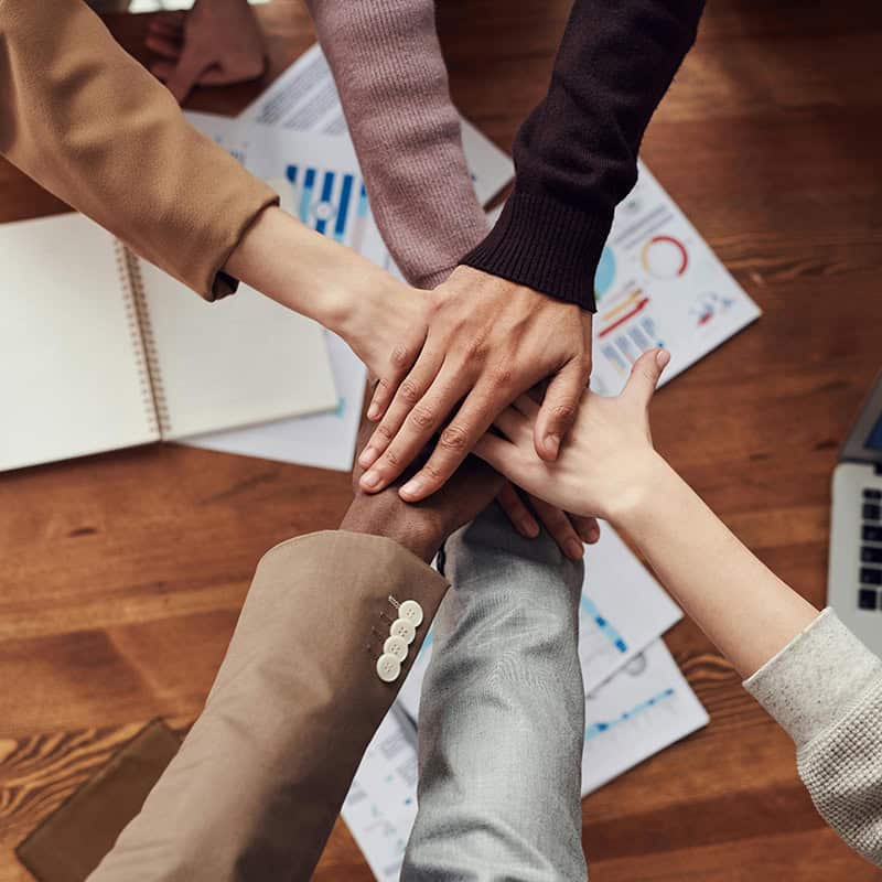 Hands of diverse team members stacked together on a wooden table, symbolizing collaboration and partnership in digital marketing strategies for local businesses and ministries.