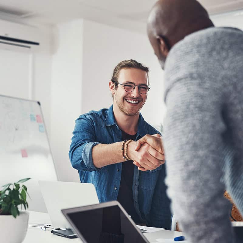 Smiling man shaking hands with another person in a modern office setting, symbolizing collaboration and partnership for local businesses and ministries.